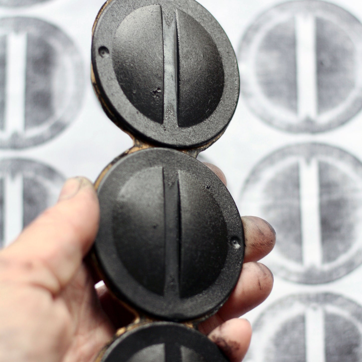 A hand holds a printing block made from found heater mounting caps, against a background of printed fabric.