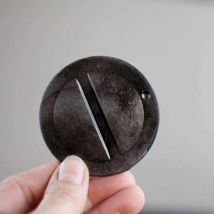 A hand holds a black plastic, discarded heater mounting cap.