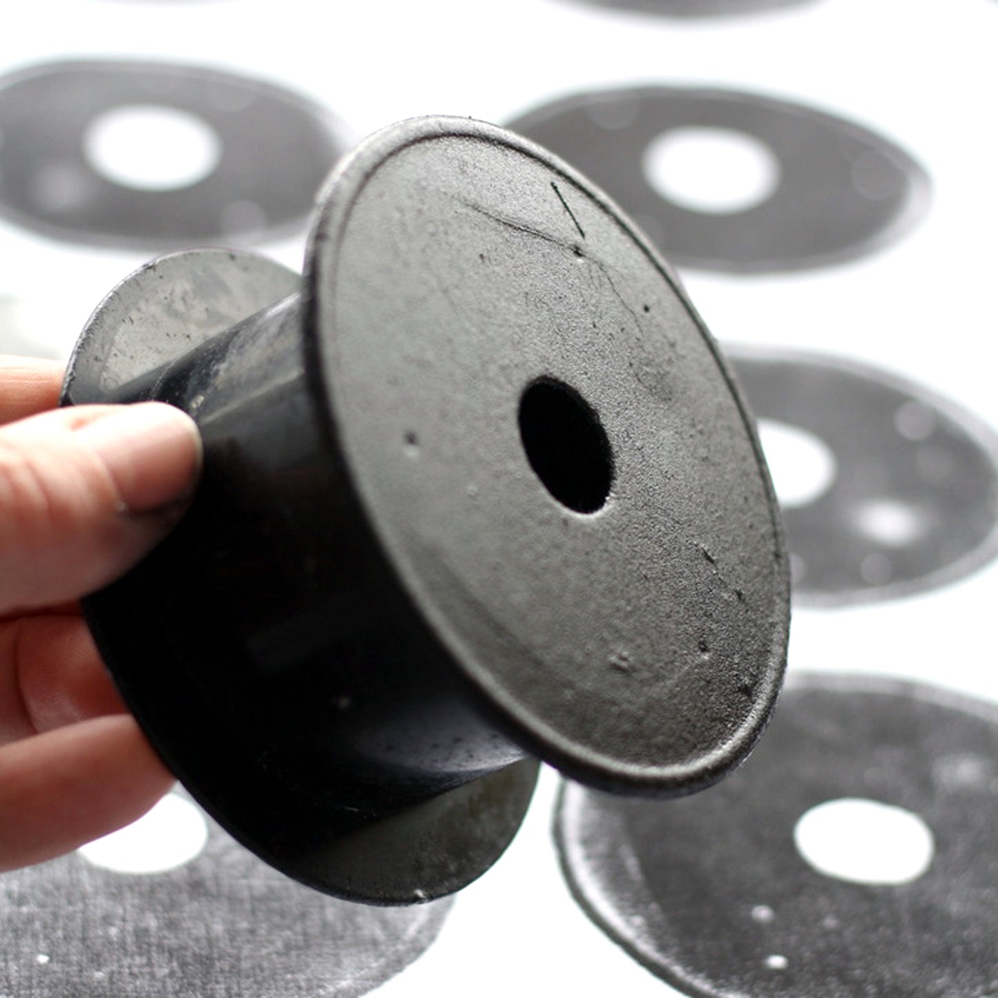 A hand holds a black plastic fishing reel against a background of hand printed black and white fabric.