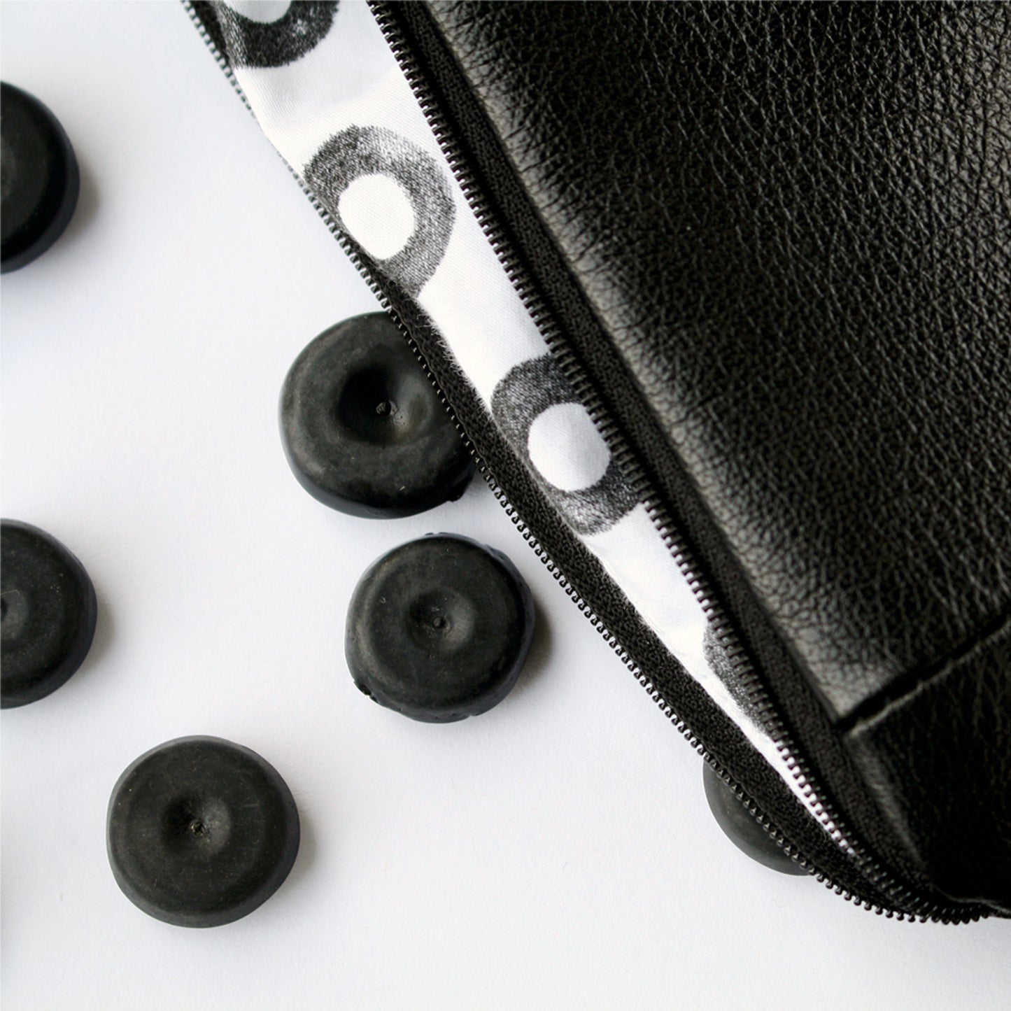 A close up image of a soft, black leather purse with hand printed lining. The lining is white cotton with small black rings on it. The purse is lying against a white surface. To the left of the image, are four small black rubber blanking plugs.