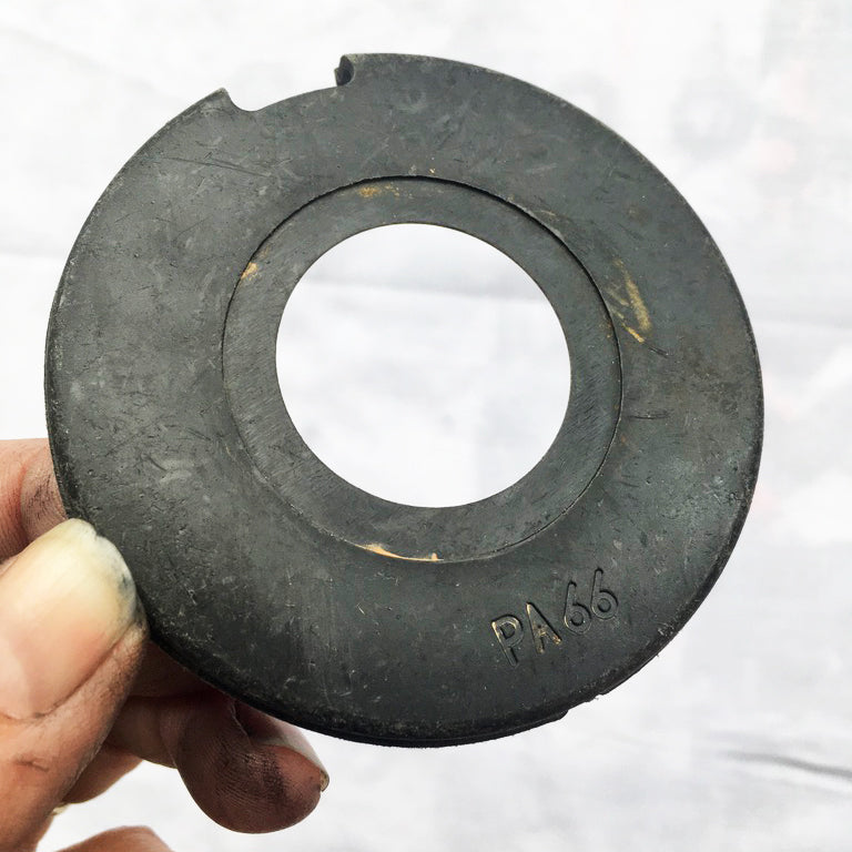 An inky hand holds a black circular plastic ring, with PA66 written on it.