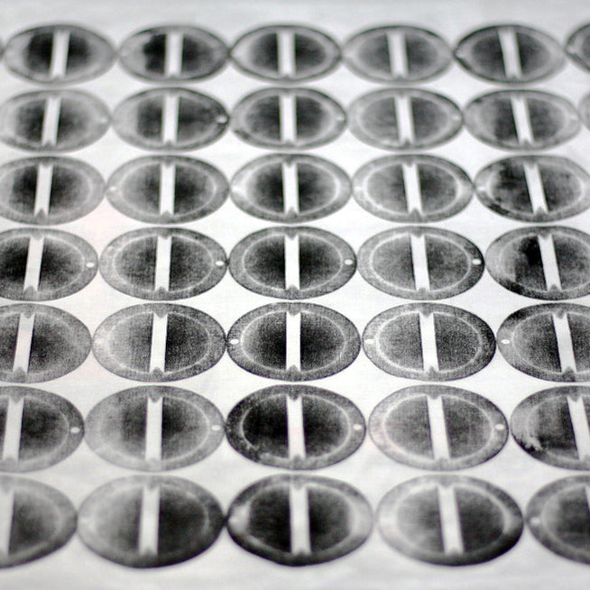 Close up detail of hand printed fabric. The print features columns of circular discs, in varying shades of black.