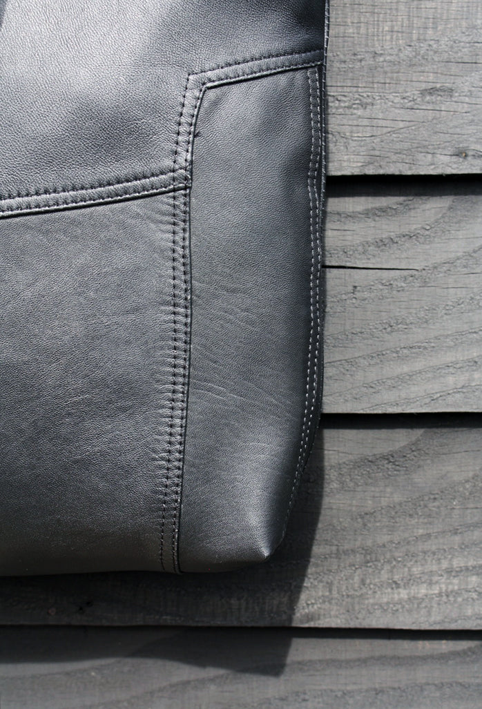 A close up detail of a soft black leather bag, against a black painted wooden surface. The image focusses on the original stitching on the leather.