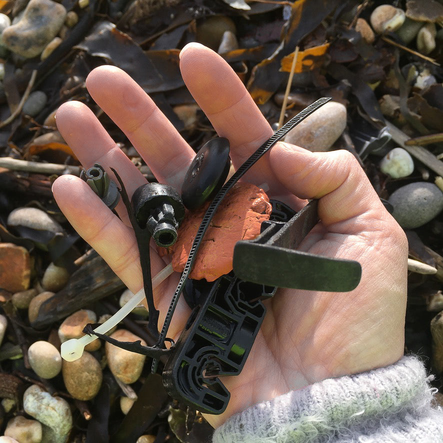 A hand holding various peices of plastic that have been washed up onto the beach, with pebbles and seaweed in the backround.