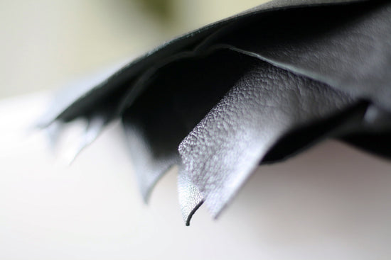 Layers of hand cut reclaimed black leather, against a white out of focus background.