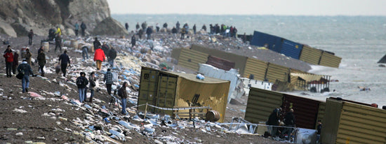 Twelve containers from the MSC Napoli cargo spill, can be seen lying on their sides on a pebble beach. Some have torn open. The contents of the containers are strew all along the length of the beach. People wearing winter clothes, walk amongst the debris.