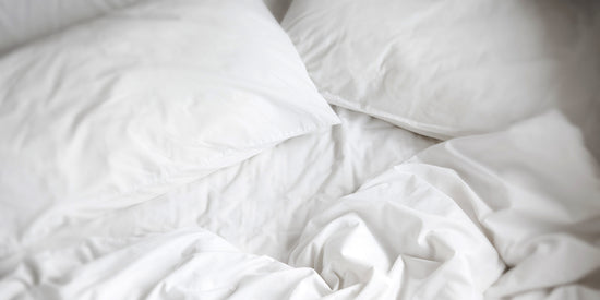 An unmade bed, with white cotton bedding.