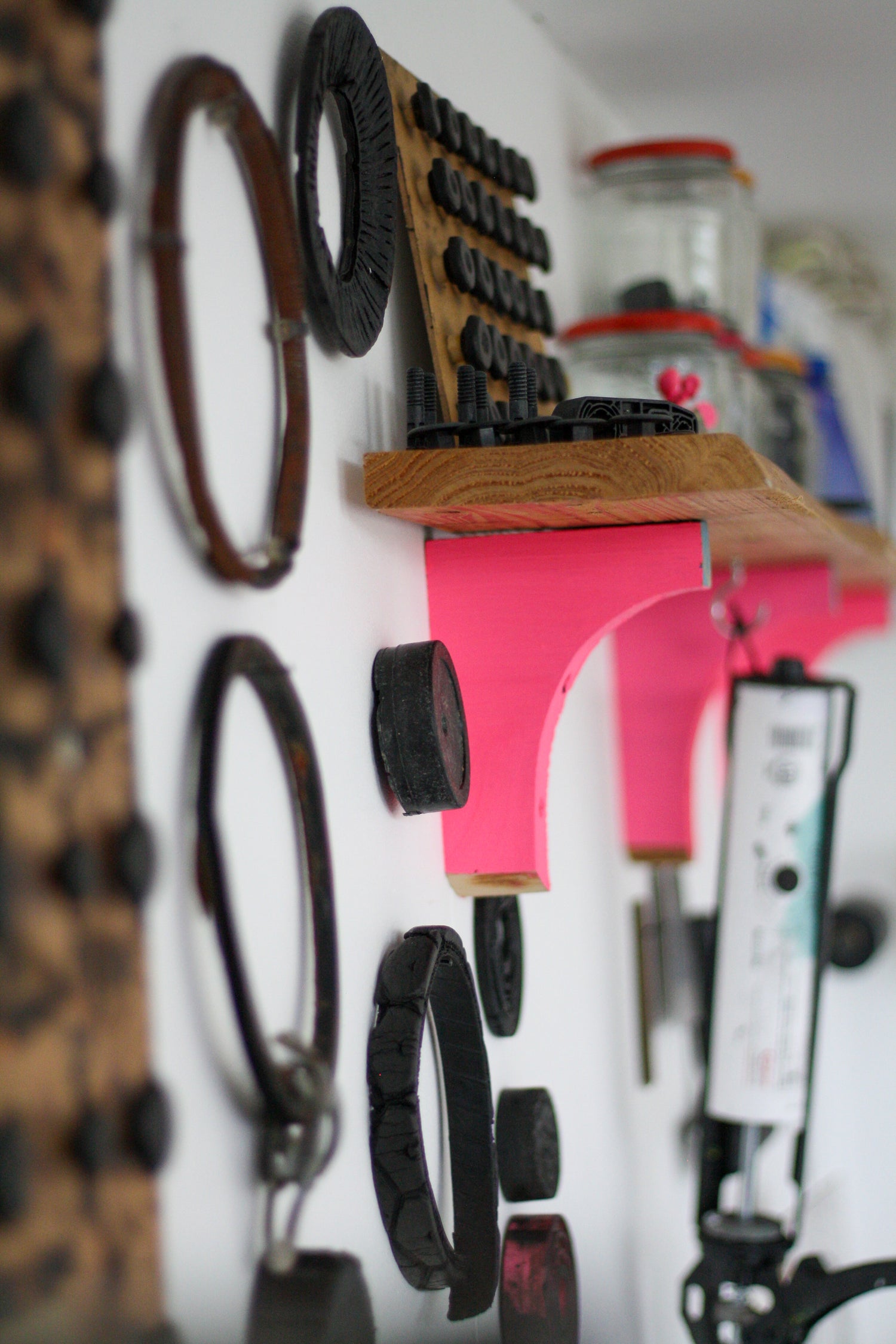 The interior of a sustainable print studio. On the ways hang various circular items found on the beach. A hand built shelf is in the back ground, with vivid pink brackets.. Jars of blanking plugs sit on the shelf.