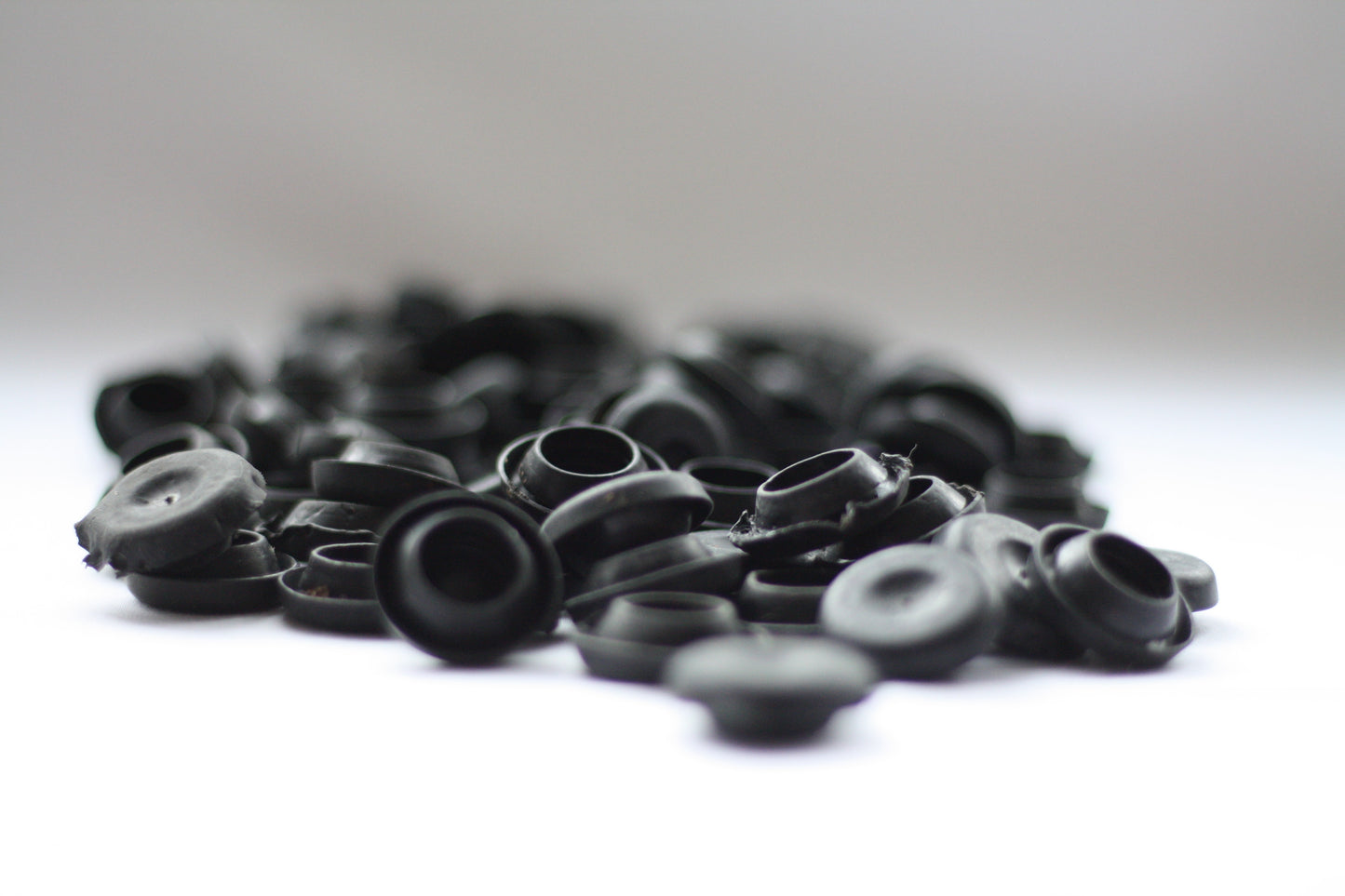 A collection of black rubber blanking plugs, sit against a white surface.