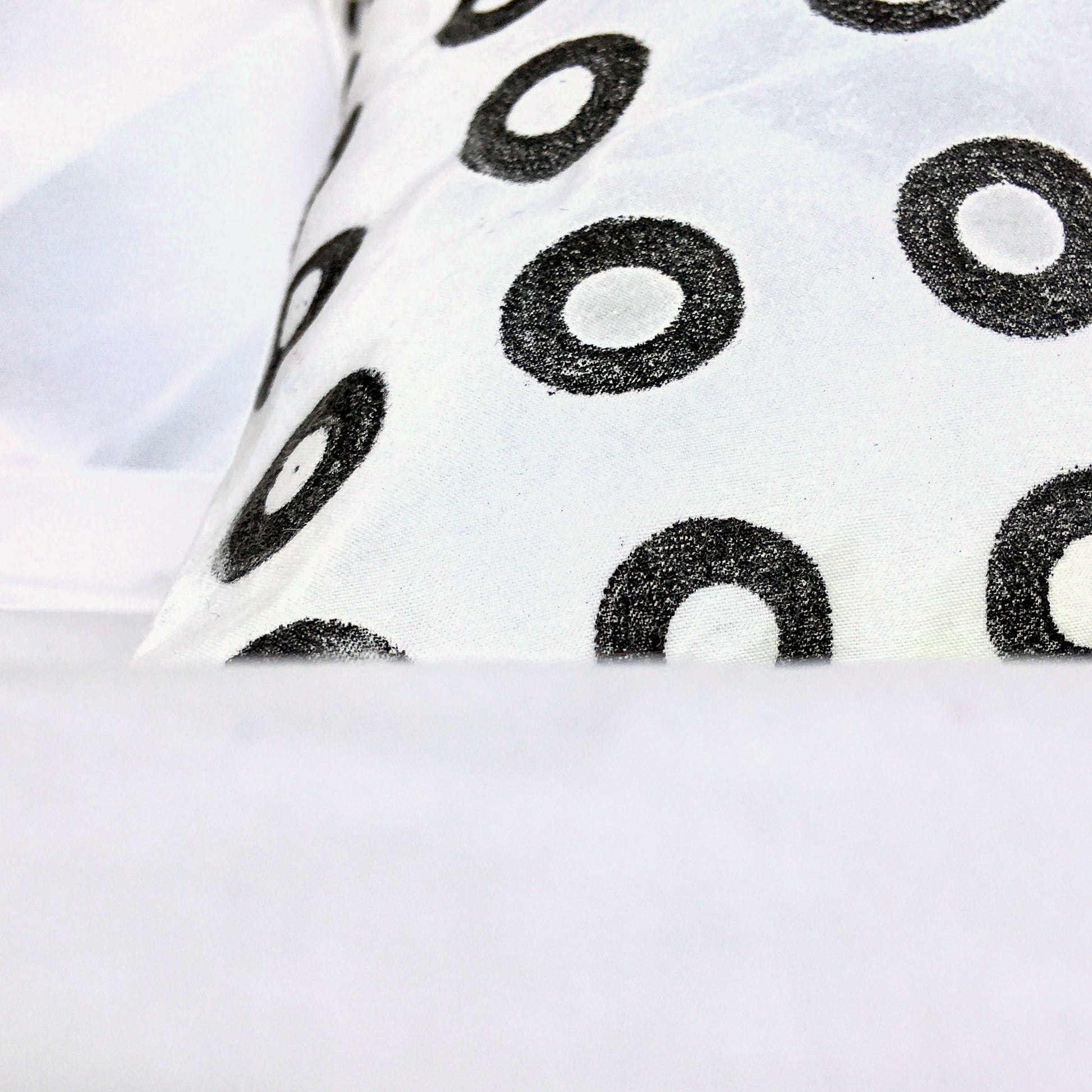 Close up image of a white sustainable, reclaimed cotton cushion, with small black, hand printed circles.