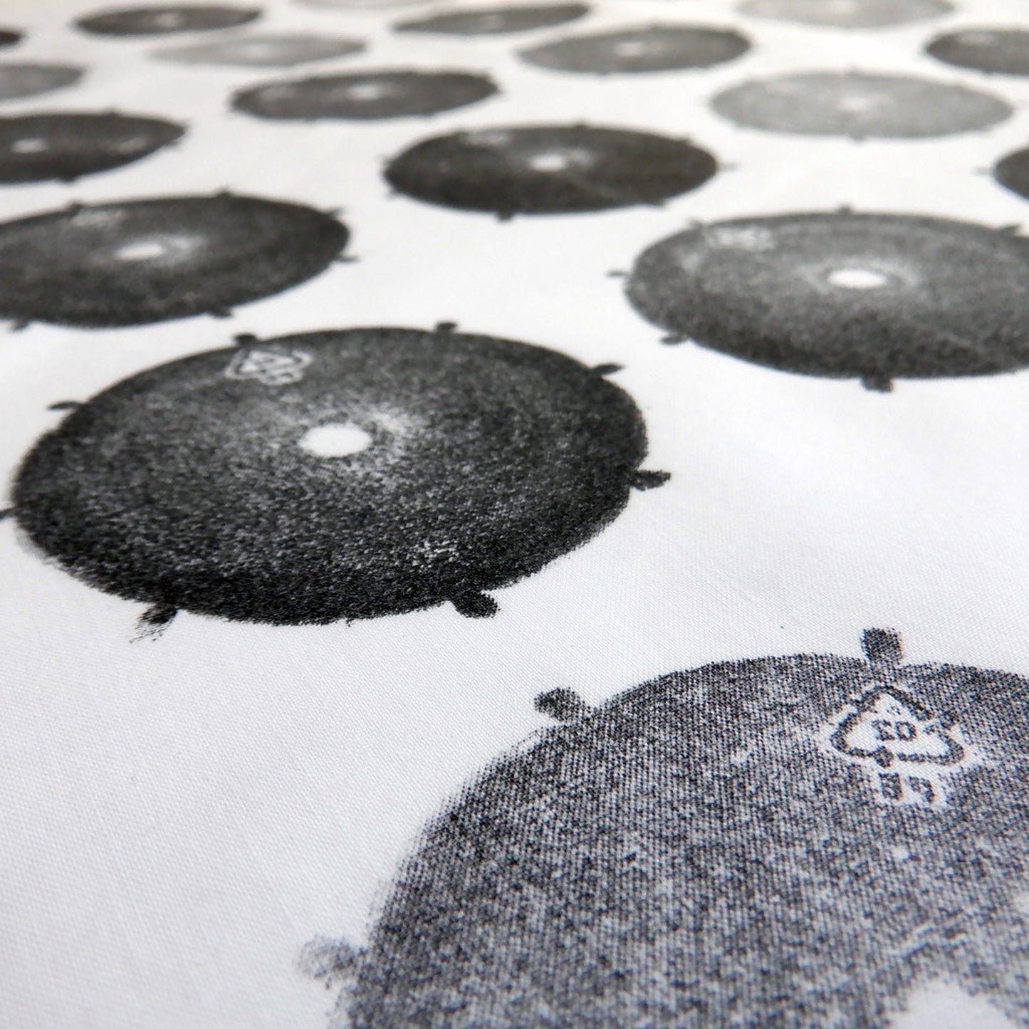 Close up printed fabric, made from a discarded plastic drum cap, in varying shades of black and grey, printed onto reclaimed white cotton.