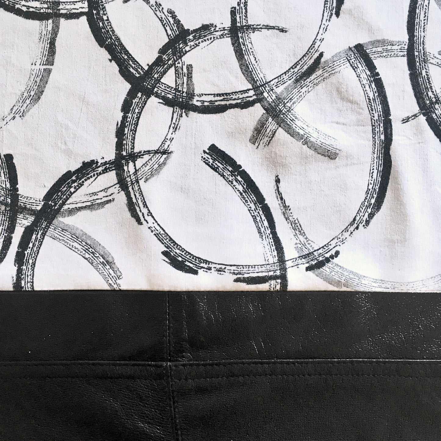 Close up detail of printed repurposed cotton and reclaimed leather tote bag, with hand printed, overlapping circles, in varying tones of black and grey.