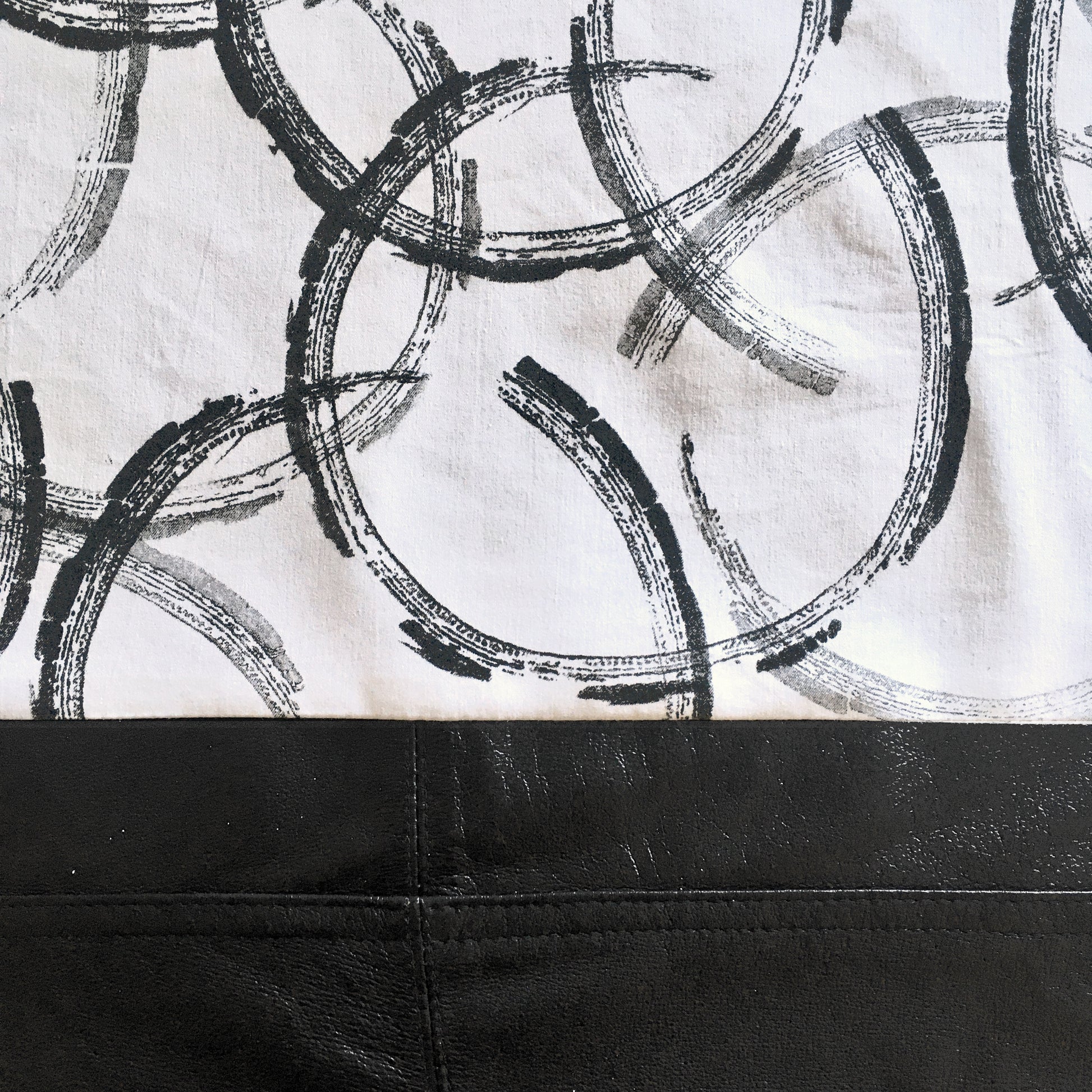 Close up detail of printed repurposed cotton and reclaimed leather tote bag, with hand printed, overlapping circles, in varying tones of black and grey.