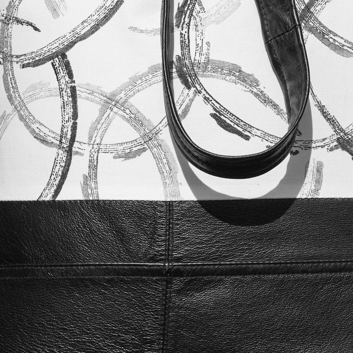 Detail of black and white, handmade reclaimed leather and hand printed cotton tote bag, with stitching detail. Black overlapping circles are printed onto white cotton.