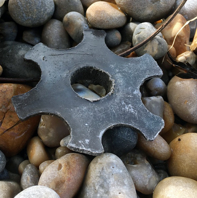 A cog shaped piece of black plastic, sits on pebbles.