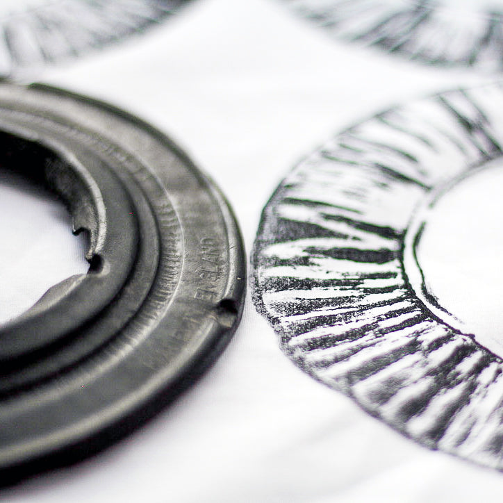 A close up image of a black rubber circle and corresponding print in black ink, against white cotton.
