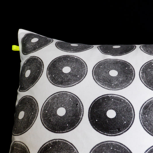 White reclaimed cushion with black printed circles, made from a discarded fishing reel. The cushion features, a small recycled polyester neon yellow tab and sits against a black background.