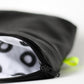 A handmade black leather purse, lies on its side, to reveal a hand printed lining. The lining is white cotton with black rings. The purse has a small neon yellow tab sewn into the side seam.