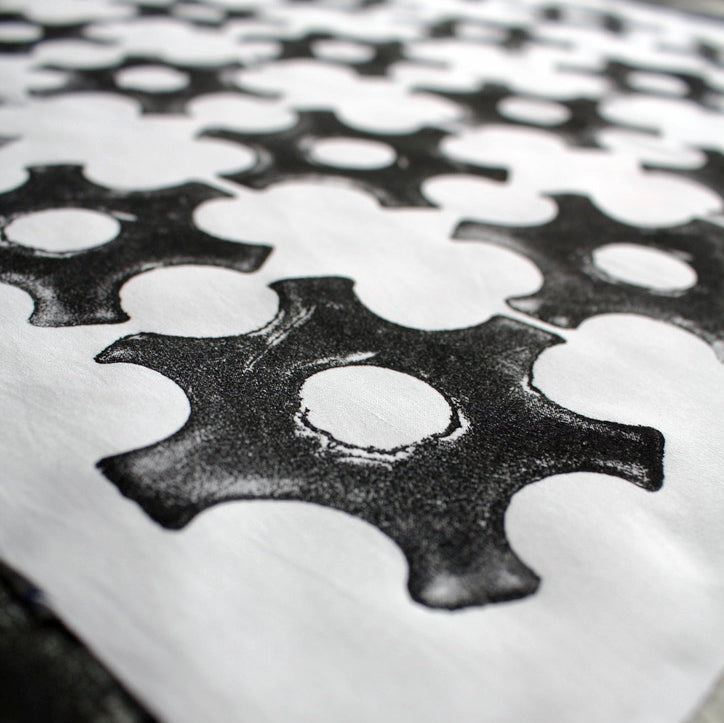 A close up of a black cog shaped repeat print, on white reclaimed cotton.